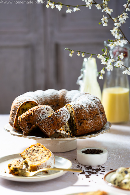 Aufgeschnittener, saftiger Eierlikör-Gugelhupf mit Schokostreuseln auf einer Kuchenplatte, bestäubt mit Puderzucker