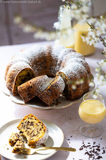 Aufgeschnittener, saftiger Eierlikör-Gugelhupf mit Schokostreuseln auf einer Kuchenplatte, bestäubt mit Puderzucker