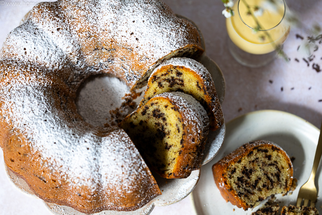 Aufgeschnittener, saftiger Eierlikör-Gugelhupf mit Schokostreuseln auf einer Kuchenplatte, bestäubt mit Puderzucker