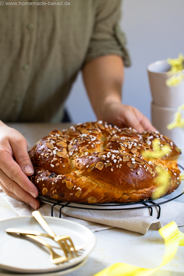 Geflochtener Osterfladen mit Mandeln und Hagelzucker wird gerade auf den Tisch gestellt.