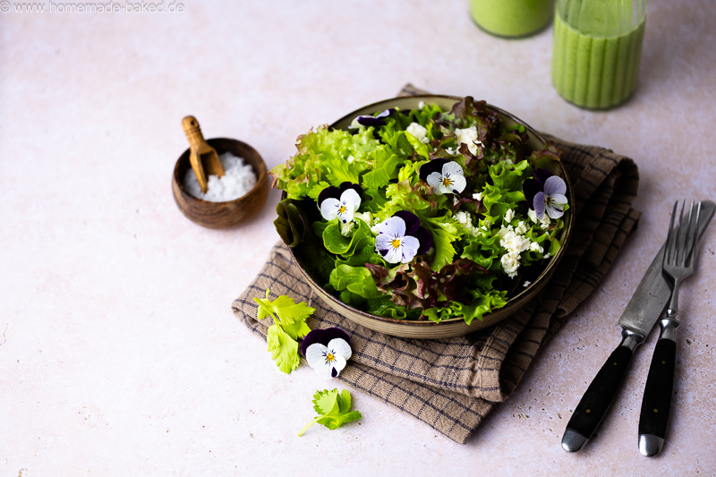 Frischer Salat mit Bärlauch-Dressing mit Buttermilch, Feta und essbaren Blumen. Daneben ein Schälchen mit Salz.