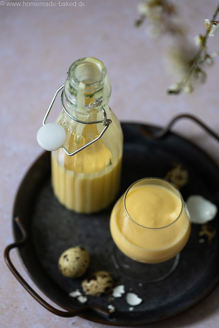 Selbstgemachter Eierlikör mit ganzen Eiern aus dem Thermomix in einer Flasche und einem Glas auf einem Tablett.