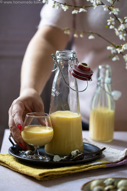 Selbstgemachter Eierlikör mit ganzen Eiern aus dem Thermomix in zwei Flaschen und einem Glas. Das Glas und eine Flasche auf einem Tablett, nach dem Glas wird gerade gegriffen