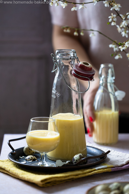 Selbstgemachter Eierlikör mit ganzen Eiern aus dem Thermomix in zwei Flaschen und einem Glas. Das Glas und eine Flasche auf einem Tablett, im Hintergrund wird die zweite Flasche in der Hand gehalten