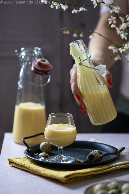 Selbstgemachter Eierlikör mit ganzen Eiern aus dem Thermomix in zwei Flaschen und einem Glas. Das Glas steht auf einem Tablett, eine Flasche mit Eierlikör wird hochgehalten
