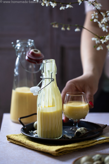 Selbstgemachter Eierlikör mit ganzen Eiern aus dem Thermomix in zwei Flaschen und einem Glas. Das Glas und eine Flasche auf einem Tablett, nach dem Glas wird gerade gegriffen
