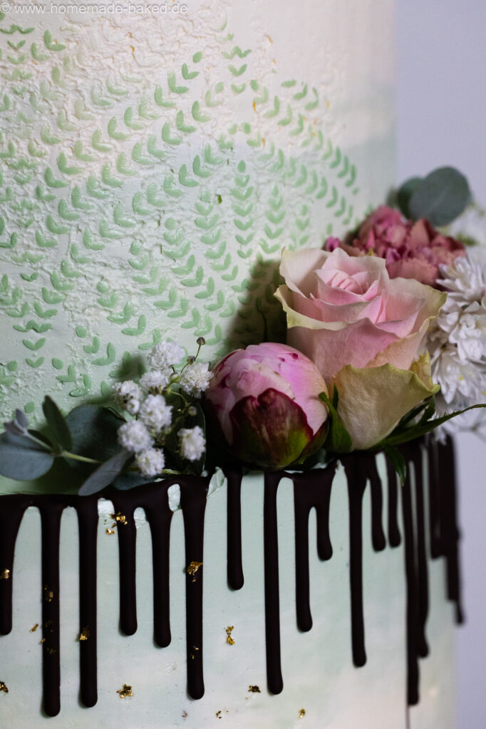 Ausschnitt einer fertig mit blumen, Blattgold und Schokodrip dekorierten dreistöckigen veganer hochzeitstorte