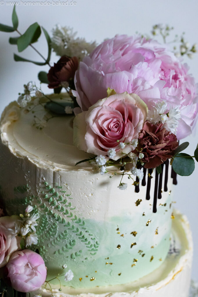 Ausschnitt einer fertig mit blumen, Blattgold und Schokodrip dekorierten dreistöckigen veganer hochzeitstorte