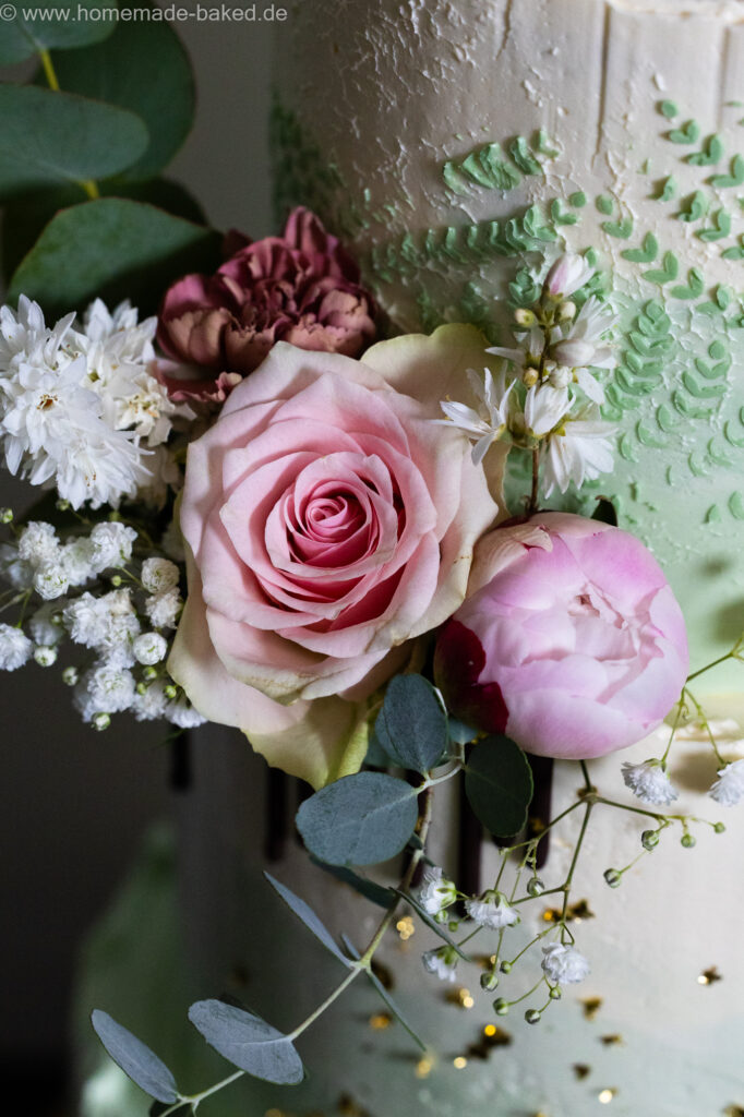 Ausschnitt einer fertig mit blumen und Blattgold dekorierten dreistöckigen veganer hochzeitstorte