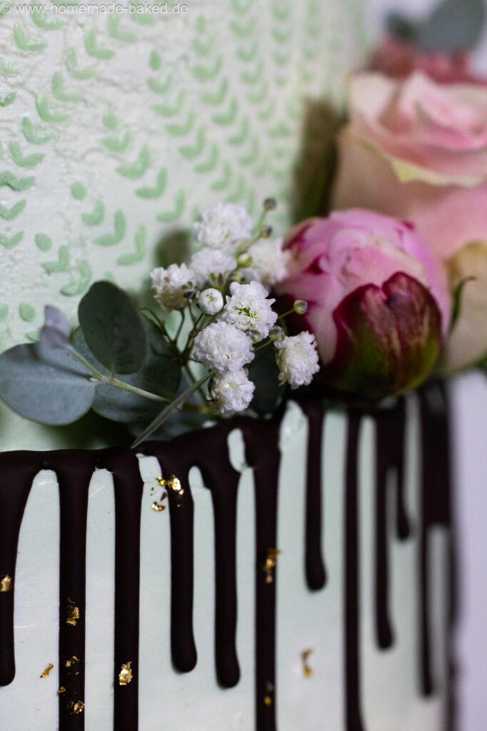 Ausschnitt einer fertig mit blumen, Blattgold und Schokodrip dekorierten dreistöckigen veganer hochzeitstorte