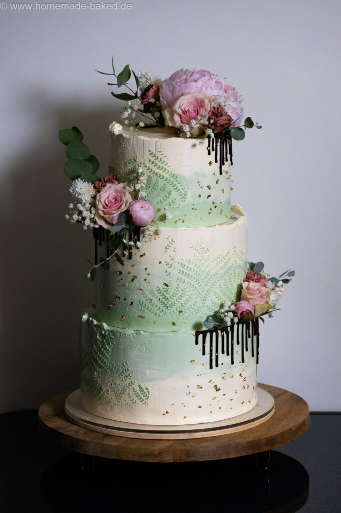 dreistöckige vegane hochzeitstorte fertig eingestrichen und mit Muster, Schokodrip, Blattgold und Blumen dekoriert