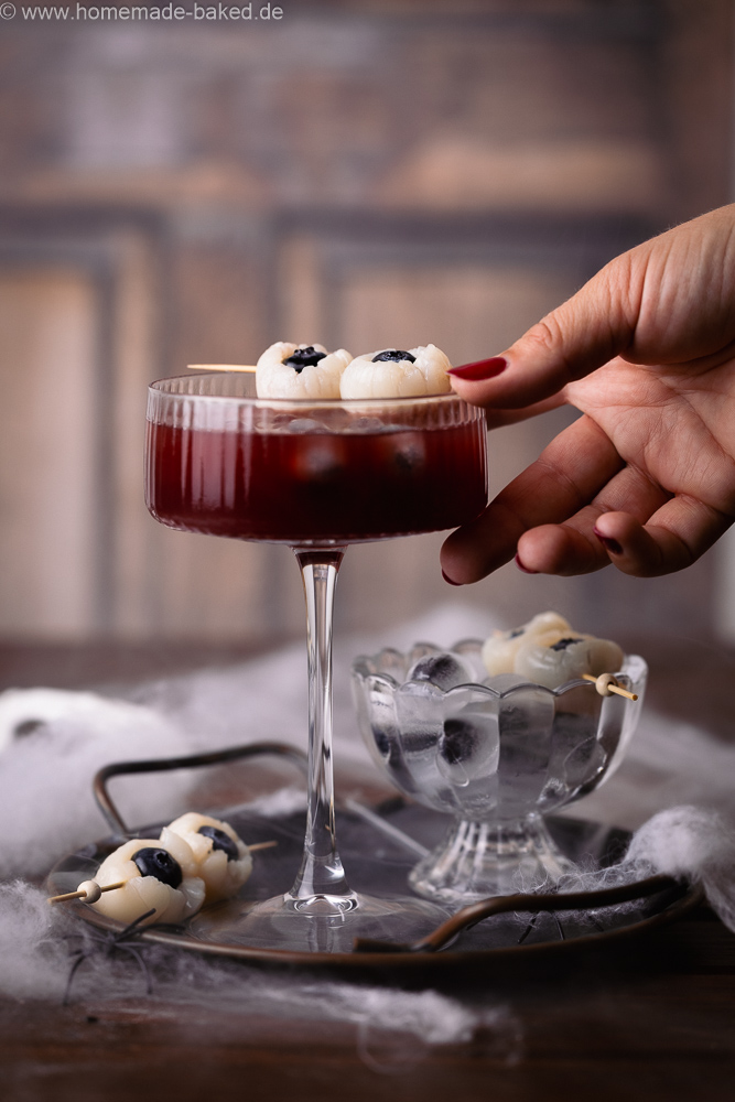 alkoholfreier halloween drink mit Augapfel-Deko, bestehend aus Litschi und heidelbeeren. Mit einer Hand wird danach gegriffen