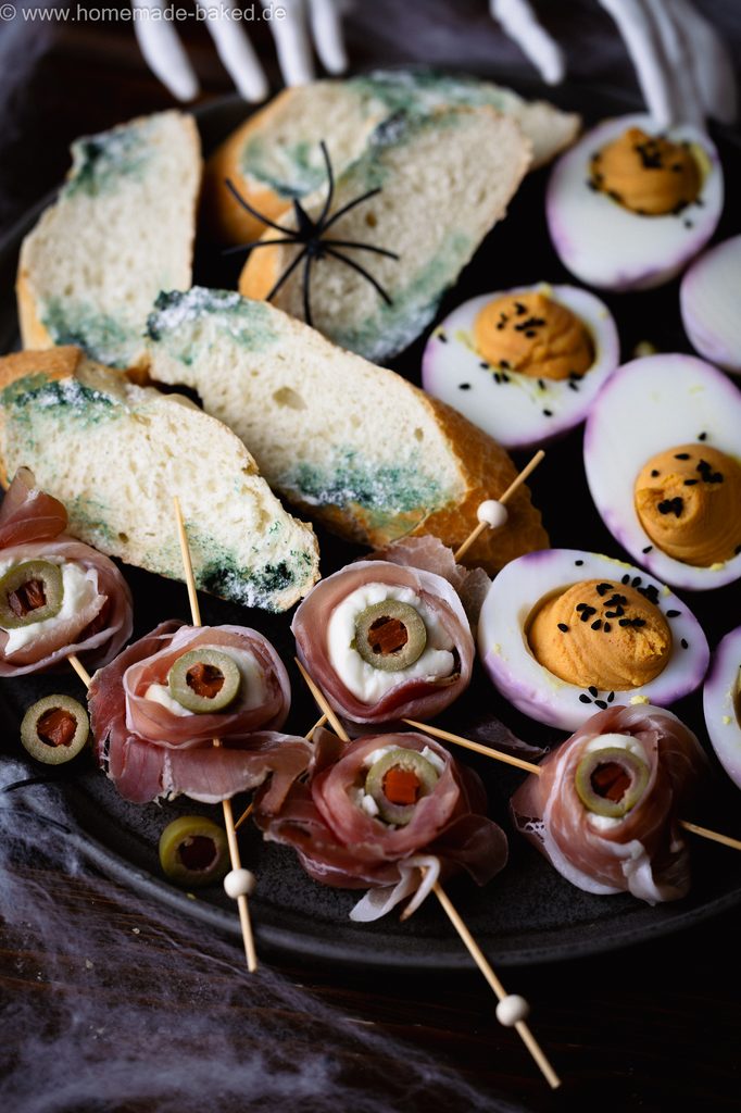 3 herzhafte Halloween Snacks auf eiiner Platte angerichtet: Verschimmelte Brotscheiben, Mozzarella-Augäpfel am Spieß und Gruseleier