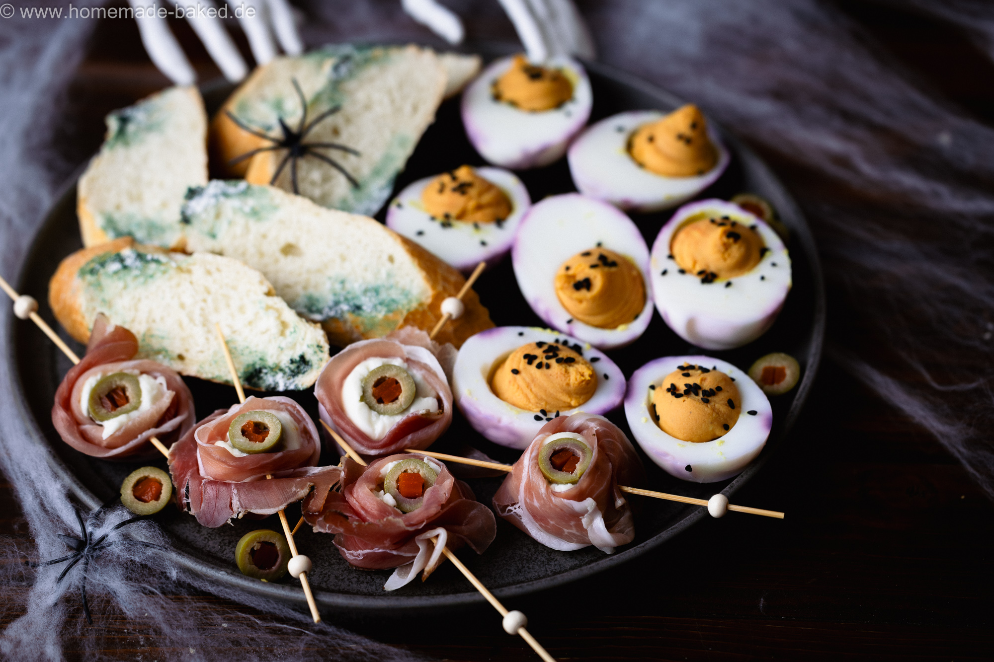 3 herzhafte Halloween Snacks auf eiiner Platte angerichtet: Verschimmelte Brotscheiben, Mozzarella-Augäpfel am Spieß und Gruseleier