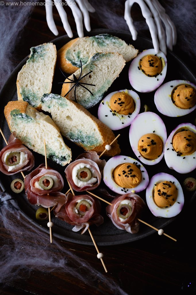 3 herzhafte Halloween Snacks auf eiiner Platte angerichtet: Verschimmelte Brotscheiben, Mozzarella-Augäpfel am Spieß und Gruseleier