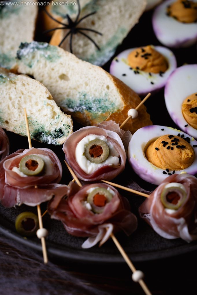 3 herzhafte Halloween Snacks auf eiiner Platte angerichtet: Verschimmelte Brotscheiben, Mozzarella-Augäpfel am Spieß und Gruseleier