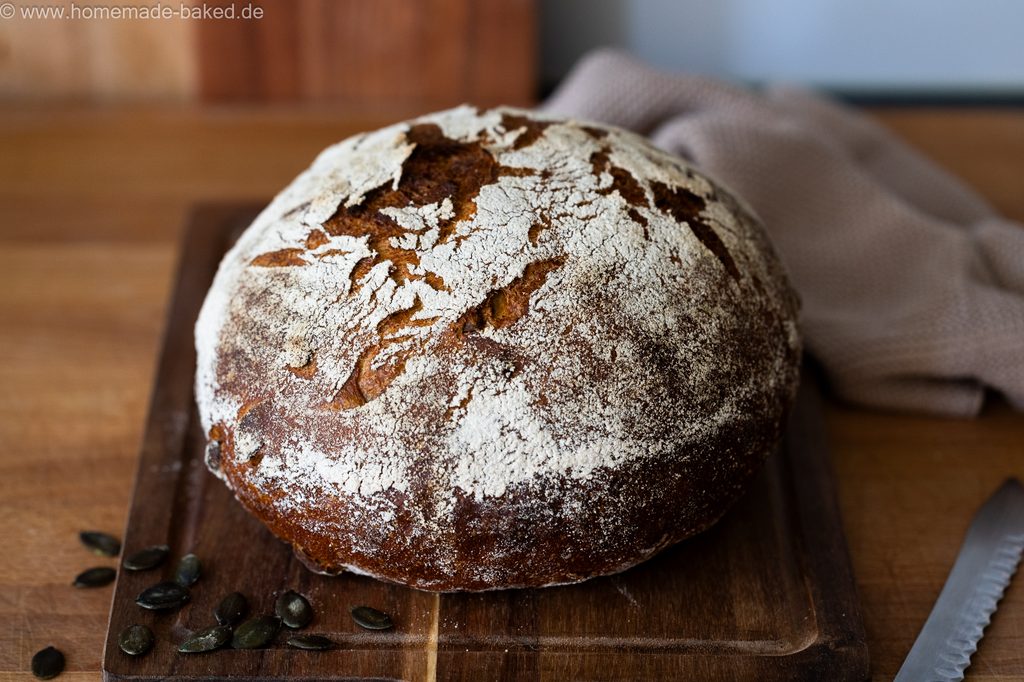 Kürbis-Sauerteigbrot im Ganzen auf einem Brett, seitlich fotografiert