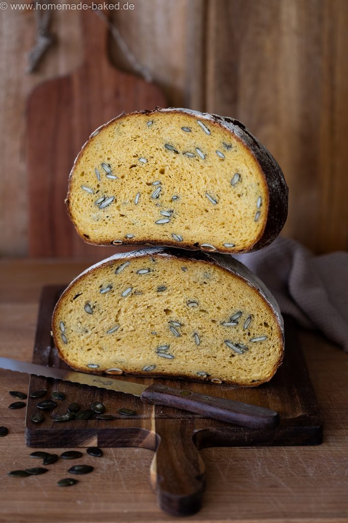 Kürbis-Sauerteigbrot mit Kürbiskerne, in der Mitte aufgeschnitten und gestapelt, so dass die saftige Krume zu sehen ist.