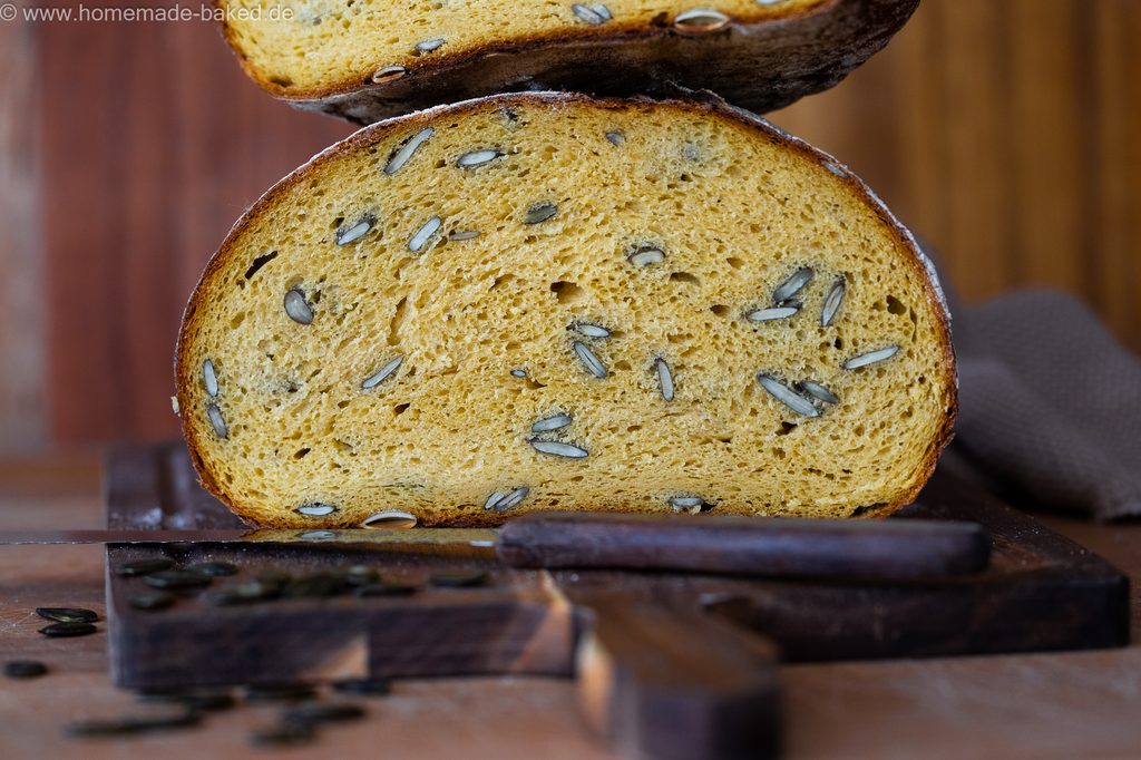 Kürbis-Sauerteigbrot mit Kürbiskerne, in der Mitte aufgeschnitten und gestapelt, so dass die saftige Krume und die Kruste gleichzeitig zu sehen sind.