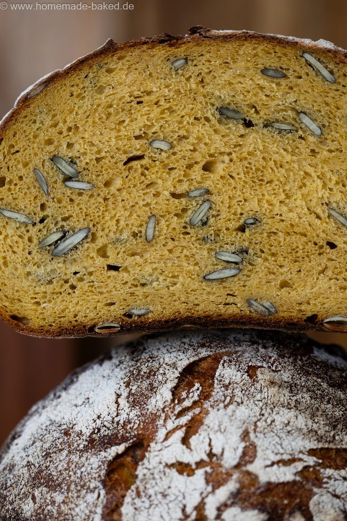 Kürbis-Sauerteigbrot mit Kürbiskerne, in der Mitte aufgeschnitten und gestapelt, so dass die saftige Krume und die Kruste gleichzeitig zu sehen sind.