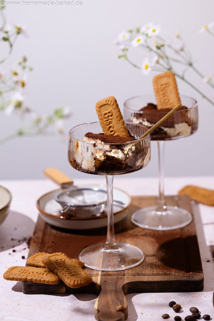 Lotus Biscoff Tiramisu im Glas, in einem hohen Champagnerkelch serviert, zwei Stück stehen hintereinander auf einem Holzbrett.