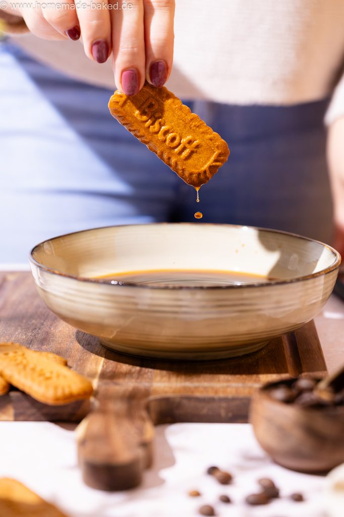 Lotus Biscoff Keks wurde gerade in Kaffee getaucht und wieder hoch genommen, man sieht Kaffee heruntertropfen.